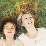 Mutter und Tochter liegen lachend im Gras