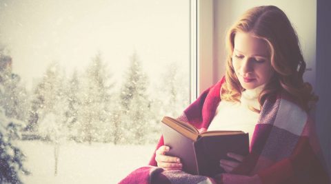 Glückliche Frau liest ein gutes Buch im Winter