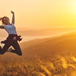 Glückliche Frau springt auf einem Feld in der Morgensonne - Gefühl von Freiheit