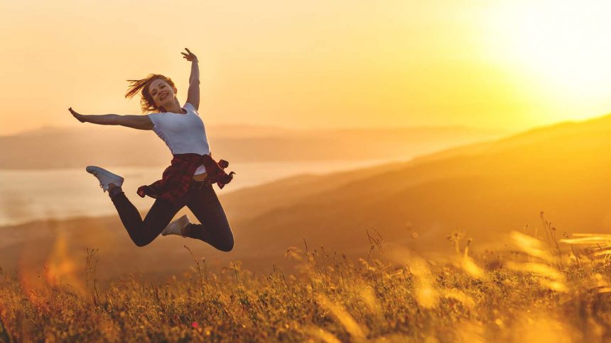 Glückliche Frau springt auf einem Feld in der Morgensonne - Gefühl von Freiheit