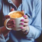 Frau mit lackierten Fingernägeln hält eine Kaffeetasse