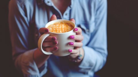 Frau mit lackierten Fingernägeln hält eine Kaffeetasse