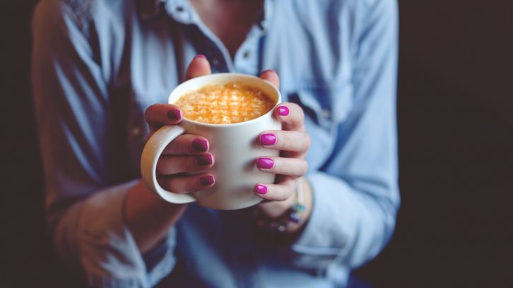 Frau mit lackierten Fingernägeln hält eine Kaffeetasse