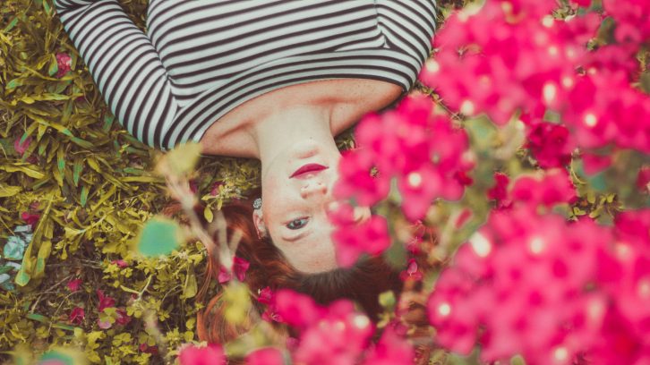 Junge Frau liegt im Frühling auf einer Wiese unter schönen roten Blüten