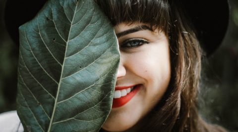 Frau versteckt ihr Gesicht hinter einem Blatt