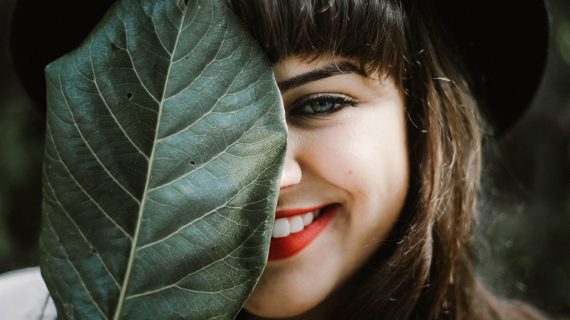 Frau versteckt ihr Gesicht hinter einem Blatt